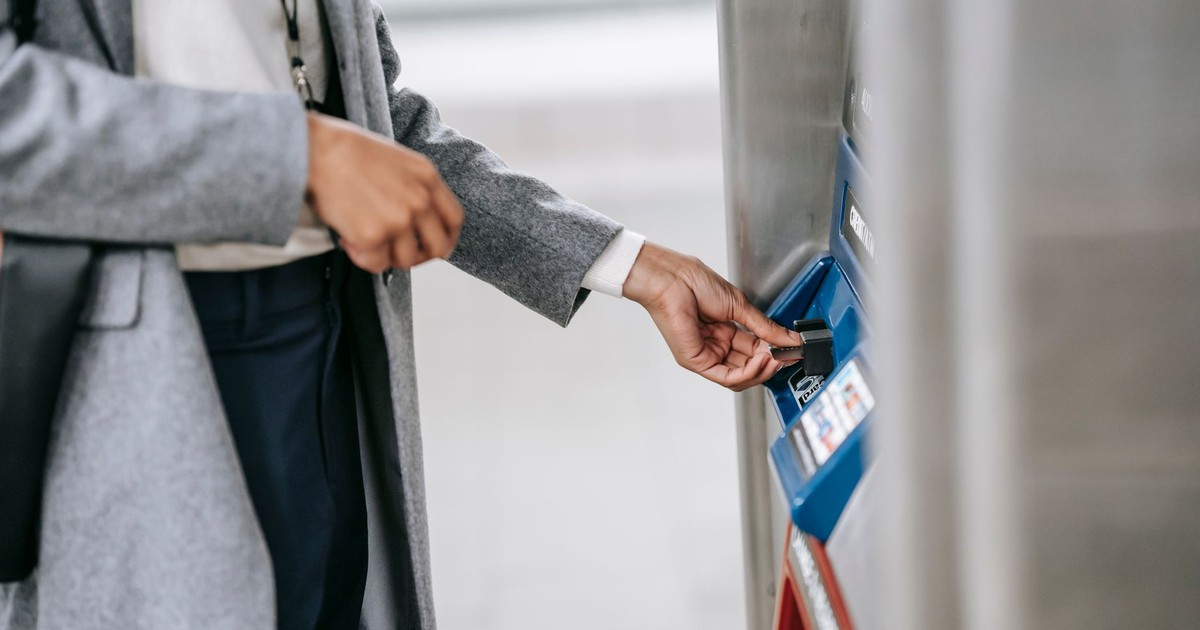 Crop unrecognizable lady in elegant clothes inserting credit card into electronic ticket machine in subway station