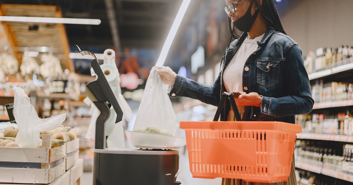 Young woman wearing a mask shops in a modern grocery store with a basket and fresh produce.