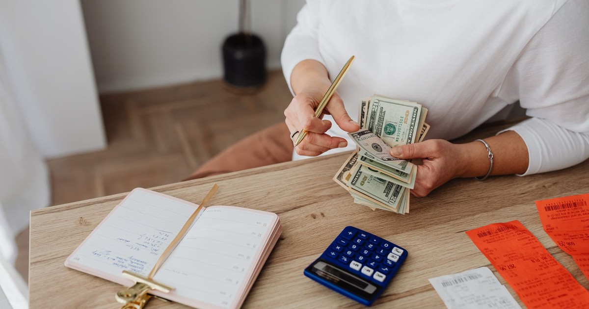Woman sorting finances with a calculator, cash, and receipts at a desk.