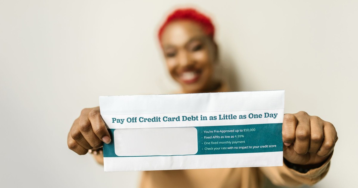Woman presenting an envelope with a credit card debt offer, blurred background.