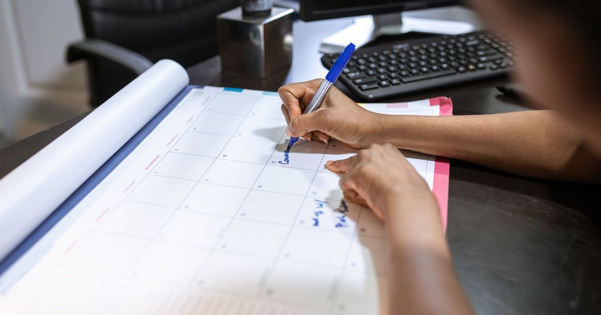 Close-up of a woman planning her schedule on a desk calendar in an office setting.