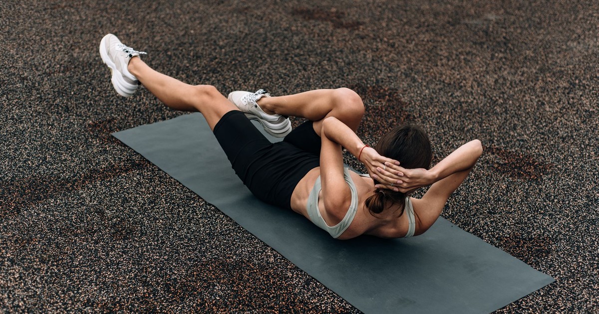 Fit woman doing a bicycle crunch on a mat outdoors, emphasizing core strength and fitness.