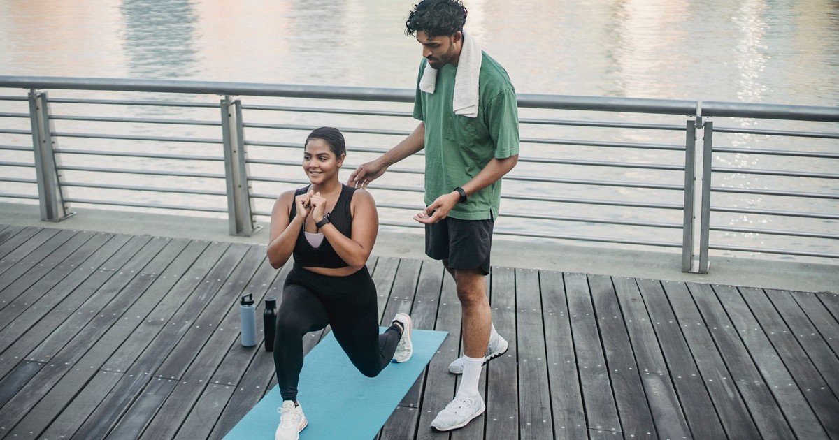 Man and woman exercising outdoors on a yoga mat by the water, promoting a healthy lifestyle.