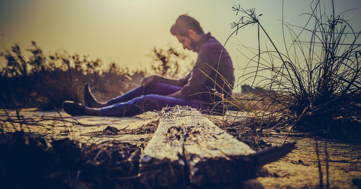 A man sits alone on sandy terrain at sunset, capturing solitude in nature's calm.