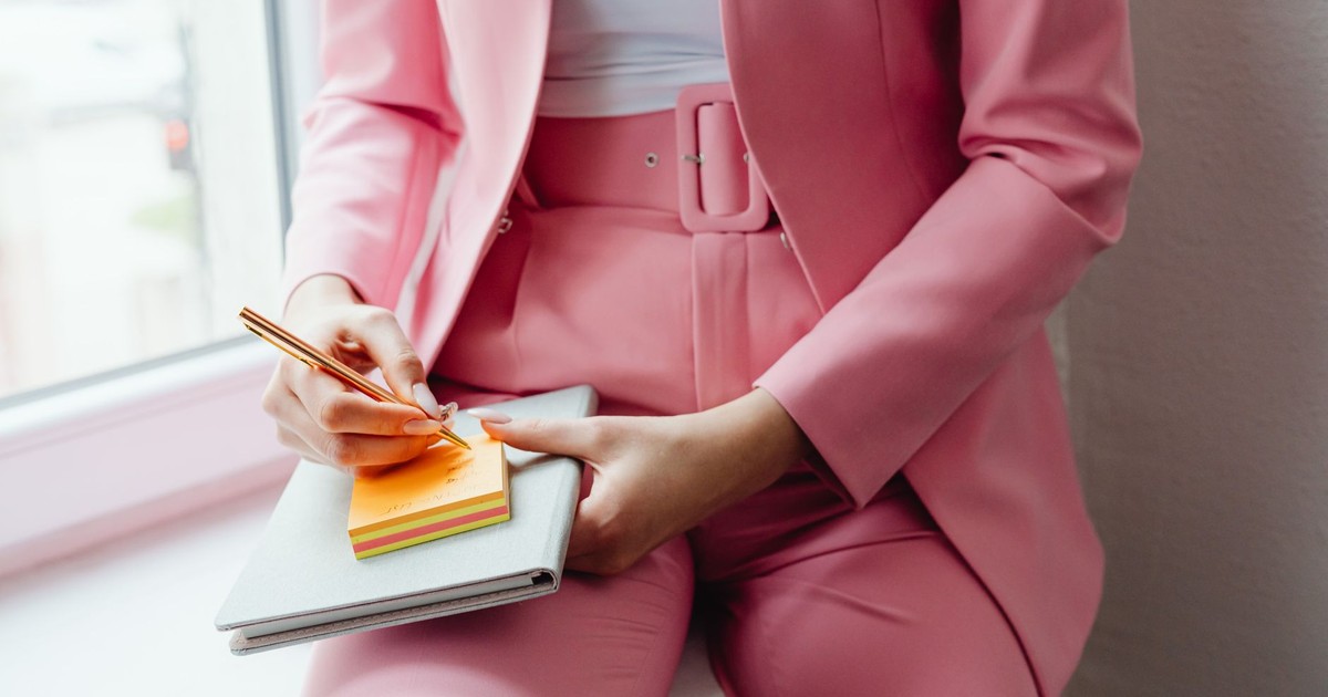 Business professional in pink suit taking notes on colorful sticky notes indoors.