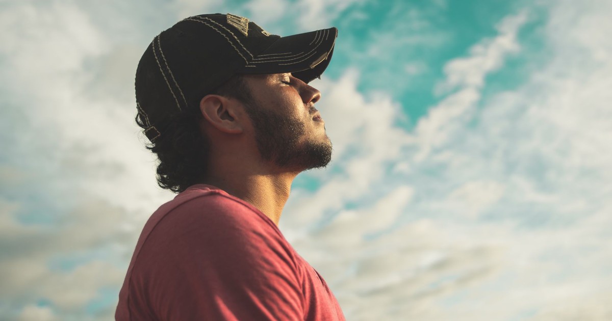 A man enjoys outdoor relaxation and mindfulness beneath a bright, cloudy sky, exuding calm and peace.
