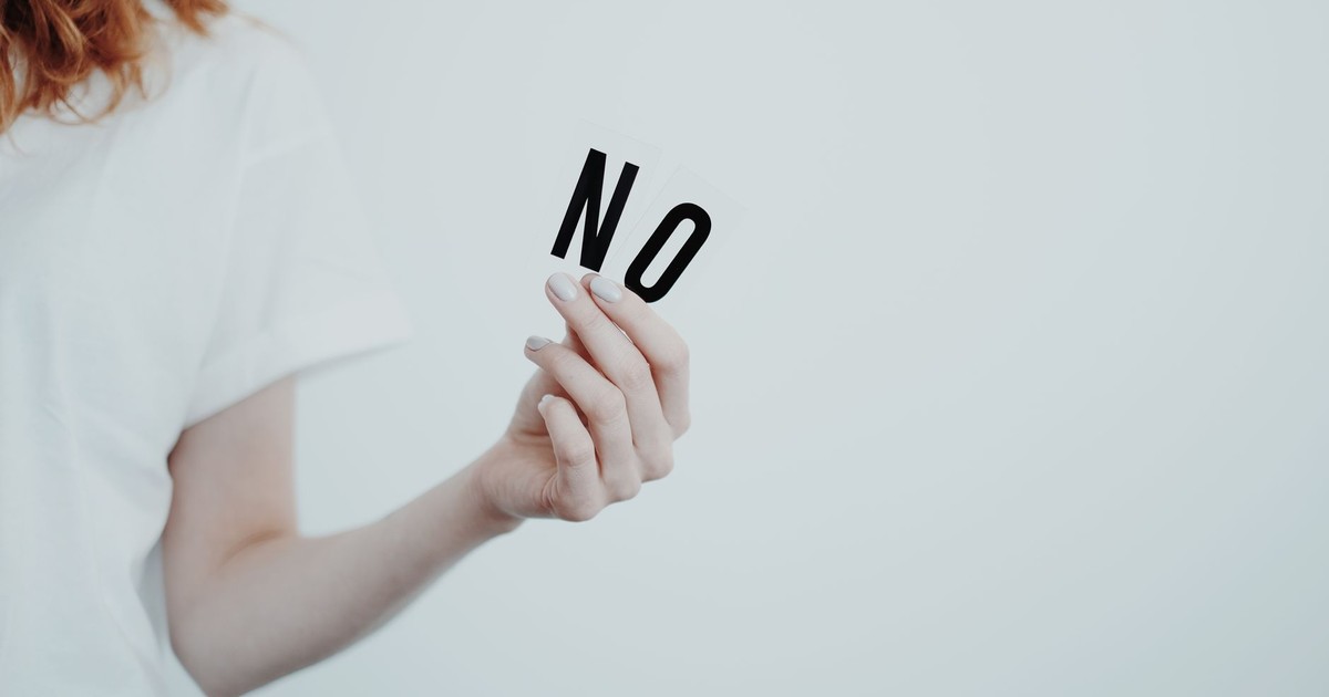 Close-up of person holding the word 'NO' in black letters on a white background, conveying a message of refusal.