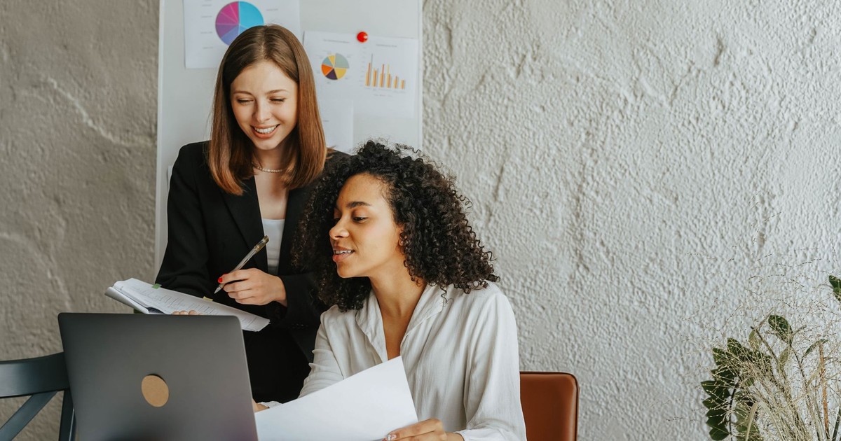 Two women discussing business strategy at the office using a laptop and charts.