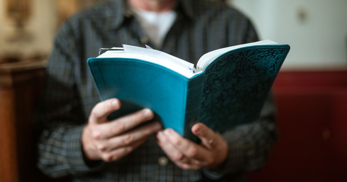 Adult man holding and reading a religious book inside a church.