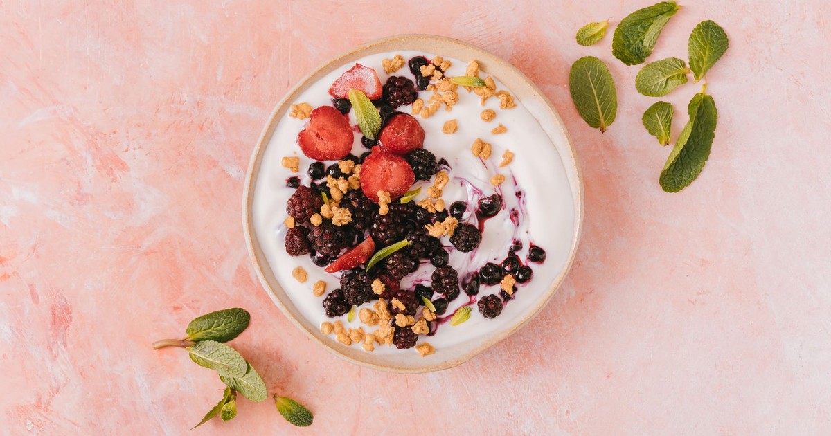 Top view of a vibrant yogurt bowl with mixed berries, granola, and mint leaves on a pink background.
