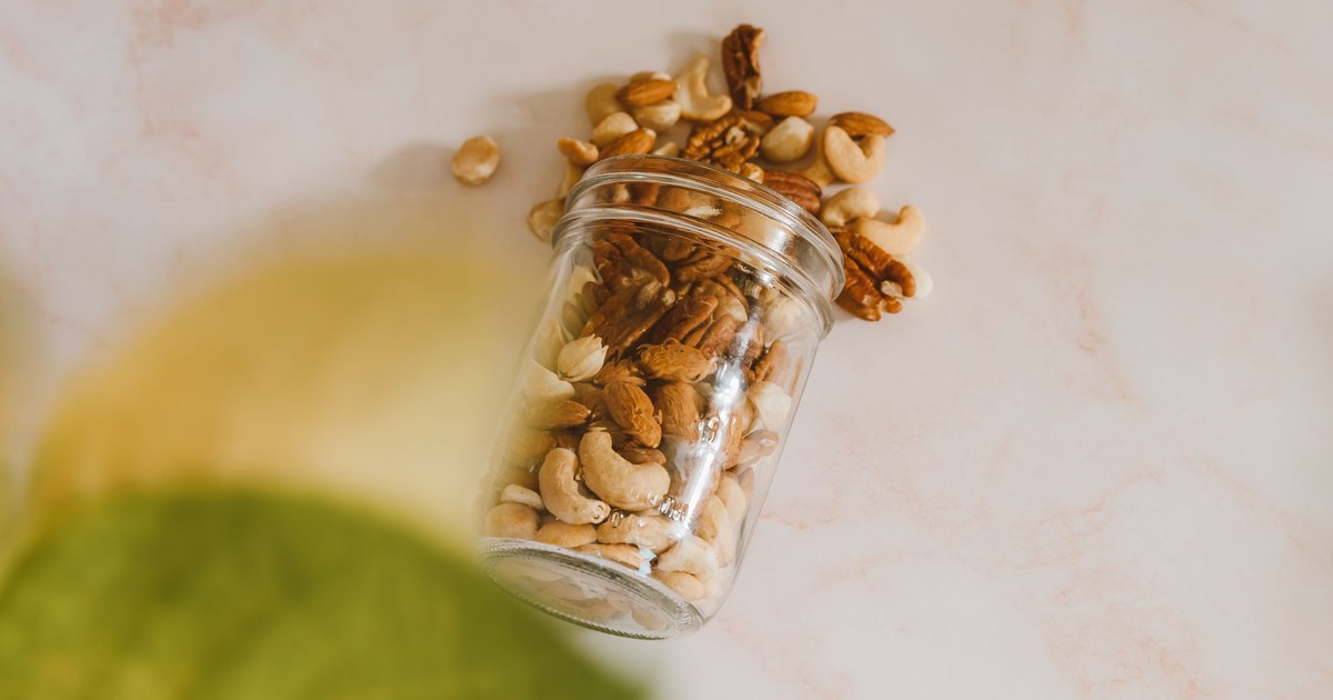 A glass jar spilling mixed nuts including cashews and almonds on a marble surface.
