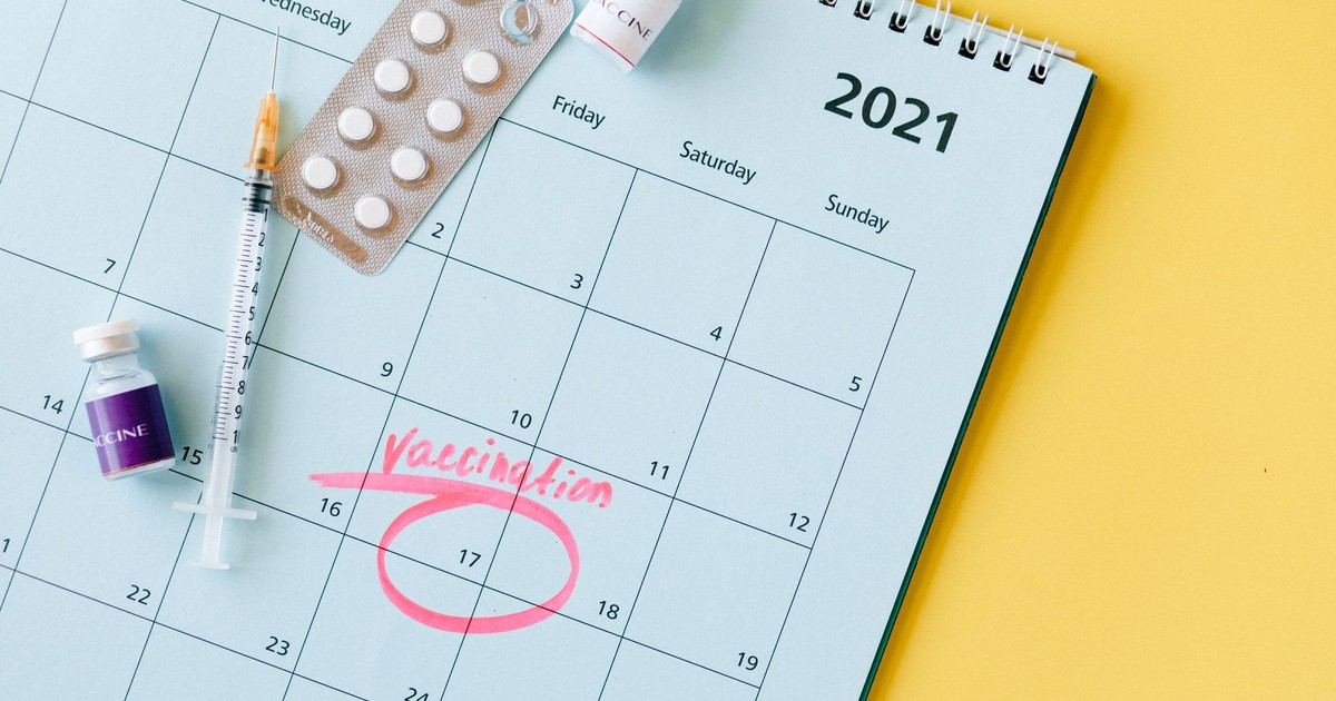 Calendar with vaccination date circled alongside vaccine vials and syringe for COVID-19 prevention.