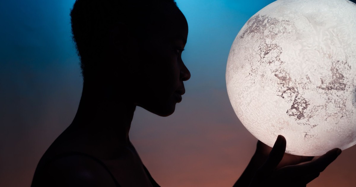 Artistic silhouette of woman holding a glowing moon globe against a vibrant backdrop.