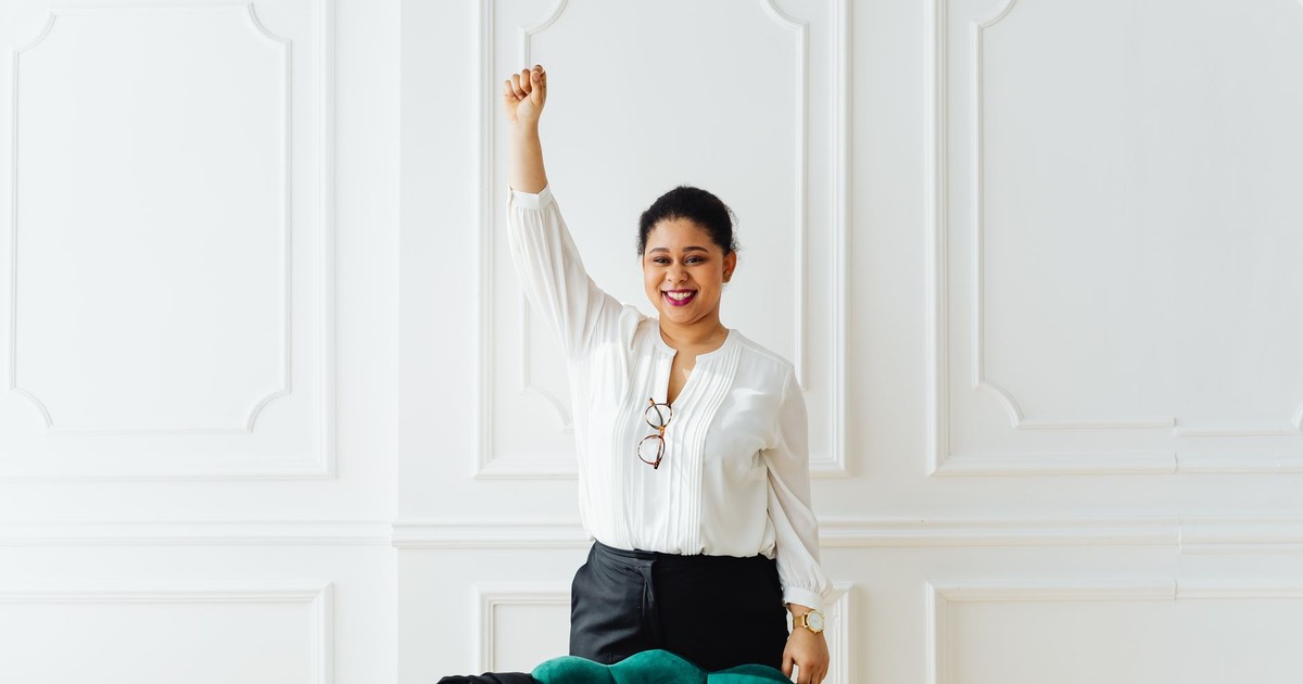 Confident woman in white blouse celebrating success with raised arm indoors.