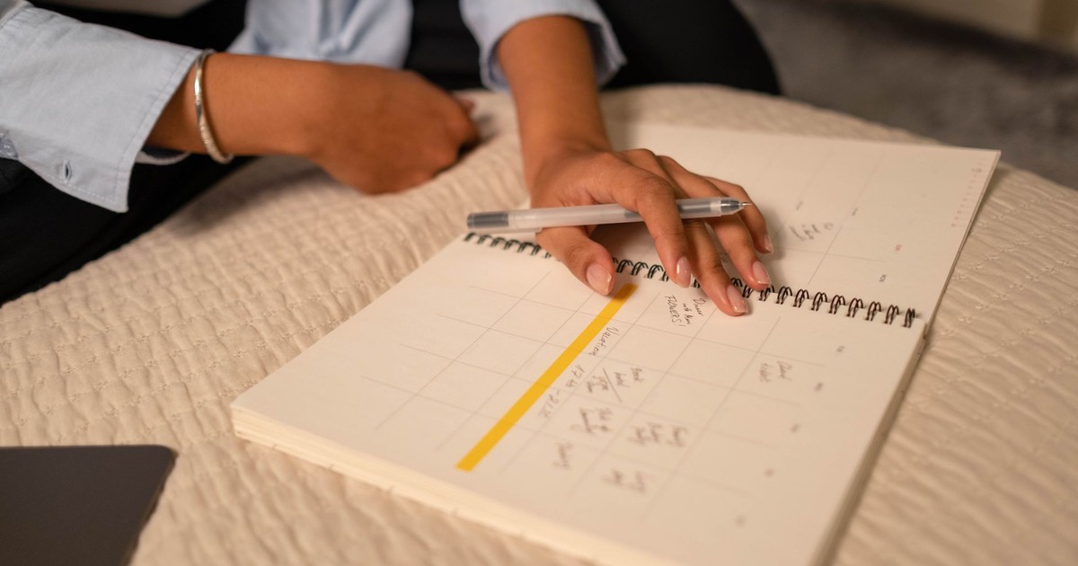 Close-up of a person scheduling in a spiral-bound planner using a pen. Indoor setting.