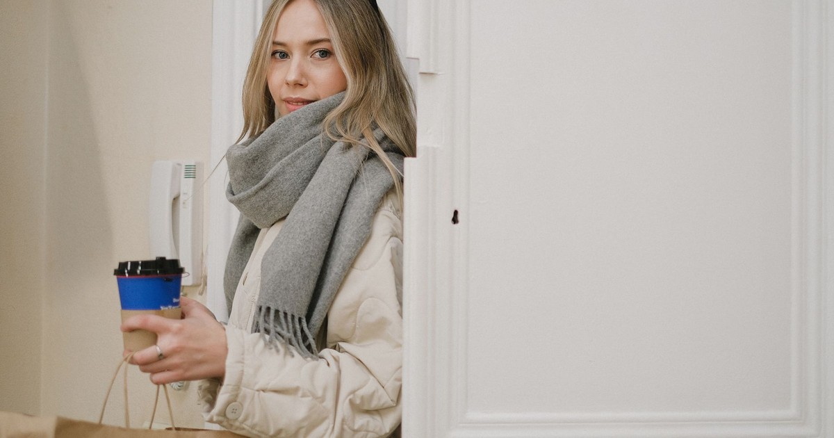 Caucasian woman indoors with coffee cup and shopping bag, dressed warmly in a scarf.