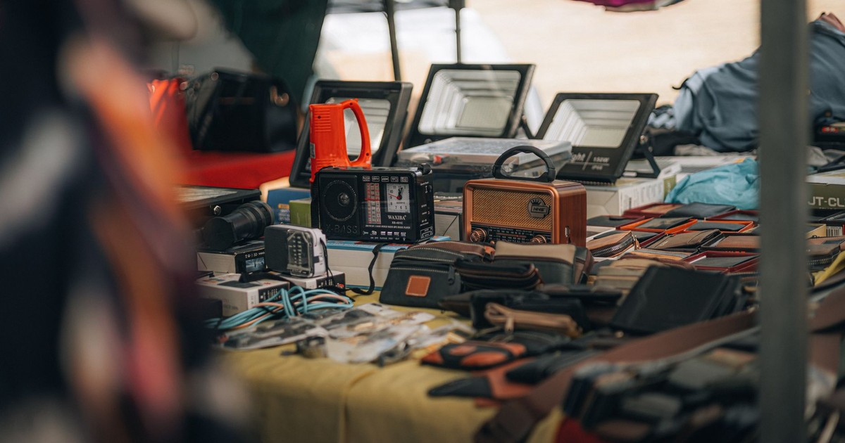 A tabletop display of vintage radios, gadgets, and leather goods at an outdoor flea market.