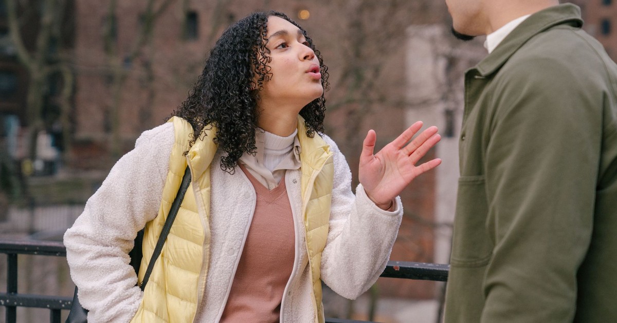 Young stylish Hispanic lady quarreling with crop boyfriend while standing together on city street