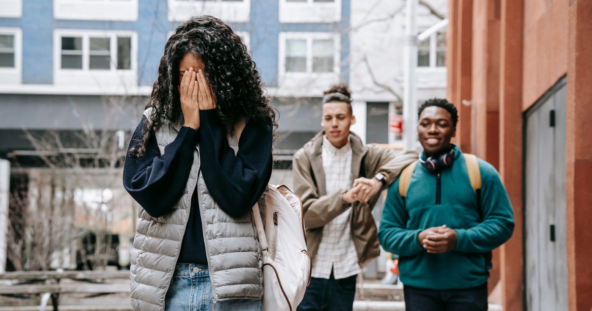 Unrecognizable young female student covering face with hands while being bullied by multiethnic male classmates on street