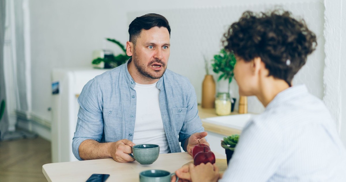 Couple having a serious conversation at the kitchen table with coffee cups.