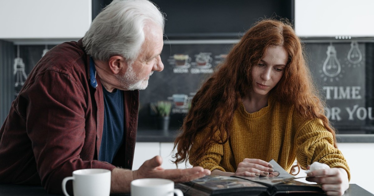 Elderly man and young woman looking at a photo album together, evoking emotions and memories.