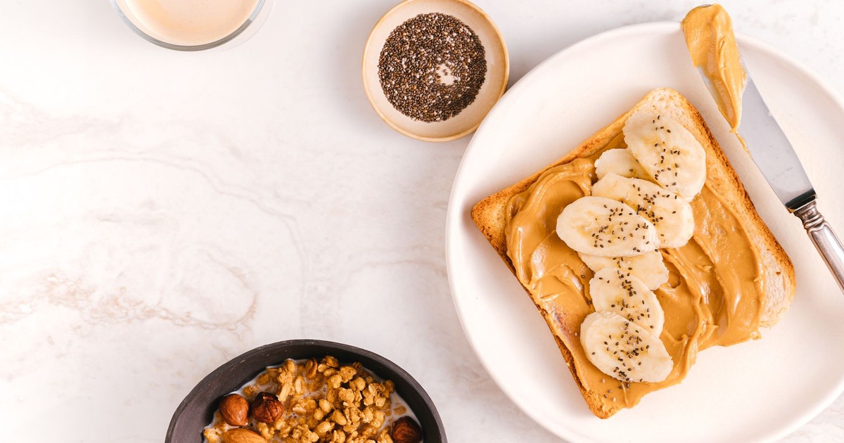 Flat lay of a nutritious breakfast featuring banana toast, chia seeds, and nuts on a marble surface.