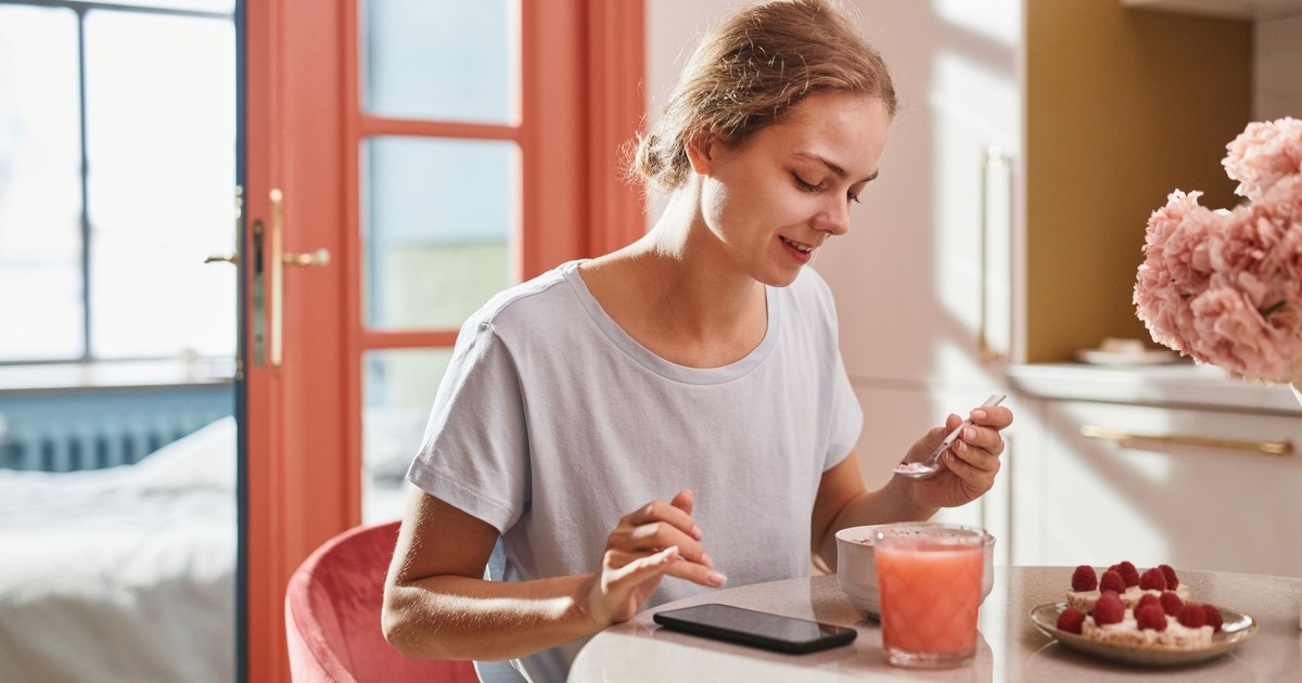 Smiling woman savoring a fresh breakfast with juice and dessert indoors.