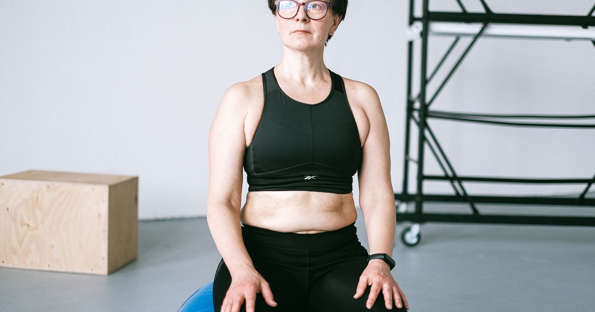 Middle-aged woman with eyeglasses exercising on a blue stability ball indoors.