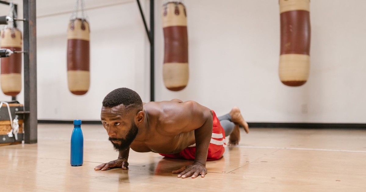 A focused shirtless man performing push-ups on a gym floor beside a blue water bottle.