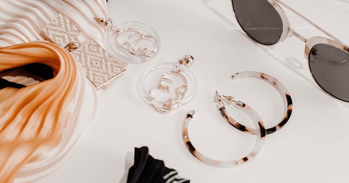 Stylish flat lay of modern fashion accessories including earrings, scarf, and sunglasses.