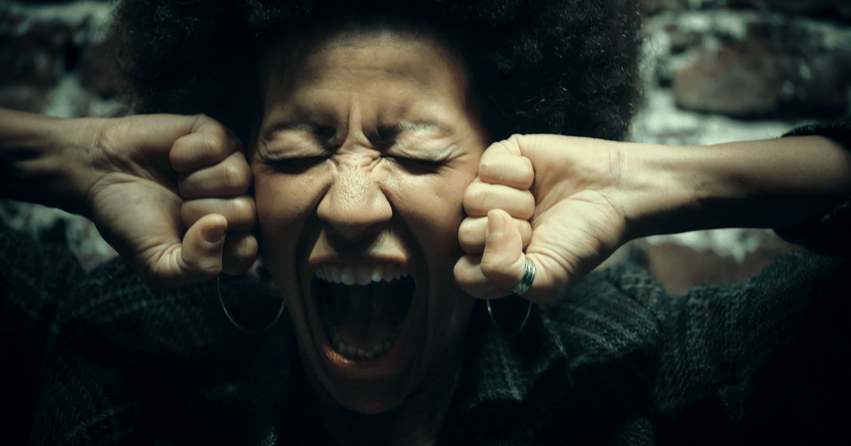 Close-up of a woman with afro hairstyle yelling with intense emotion against a brickwall.