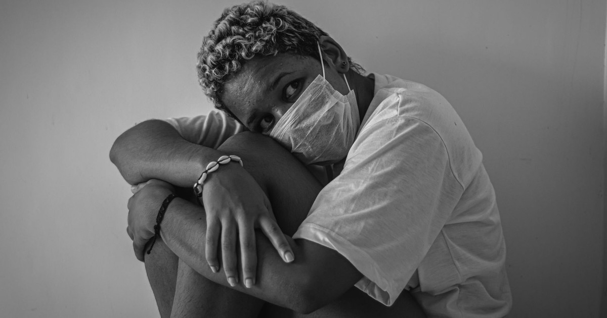 A person seated, wearing a face mask, expressing anxiety in a grayscale photograph.