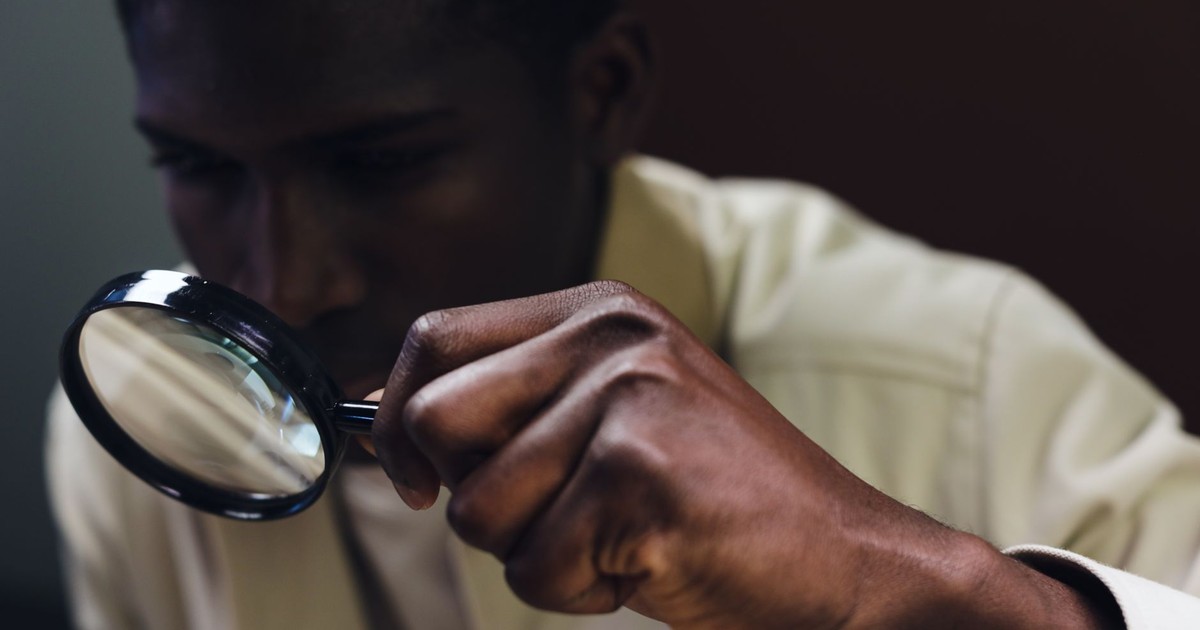 A man closely inspects an object using a magnifying glass.