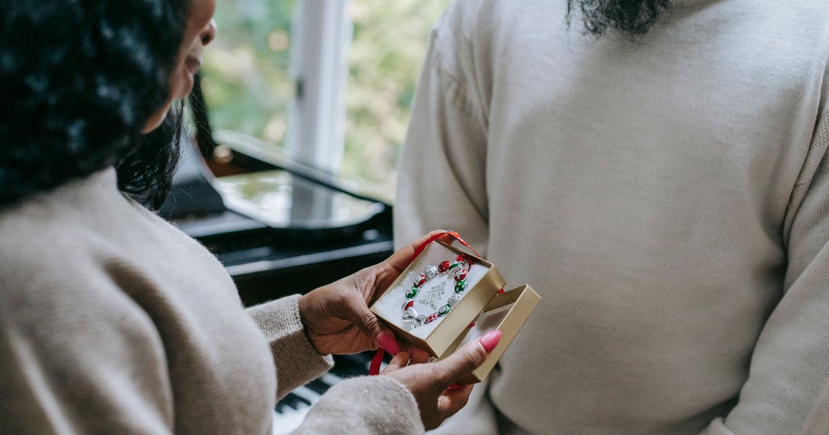 Crop anonymous happy African American couple in sweaters exchanging gifts on blurred background of home