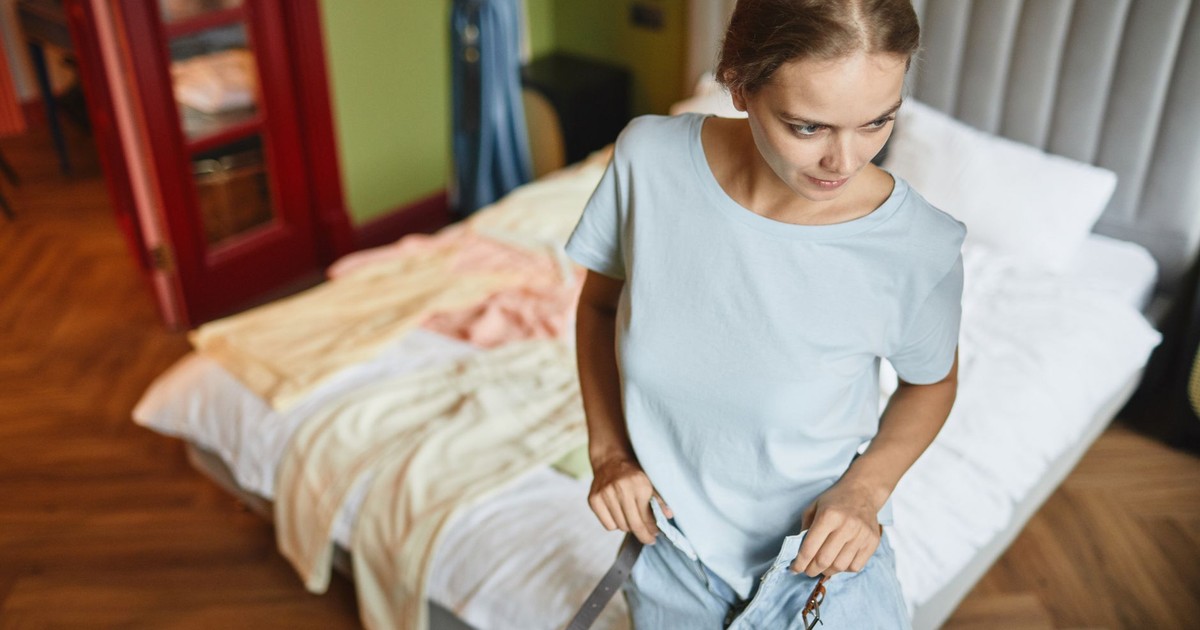 A young woman in a blue shirt dressing up in a modern bedroom, focusing on style and comfort.