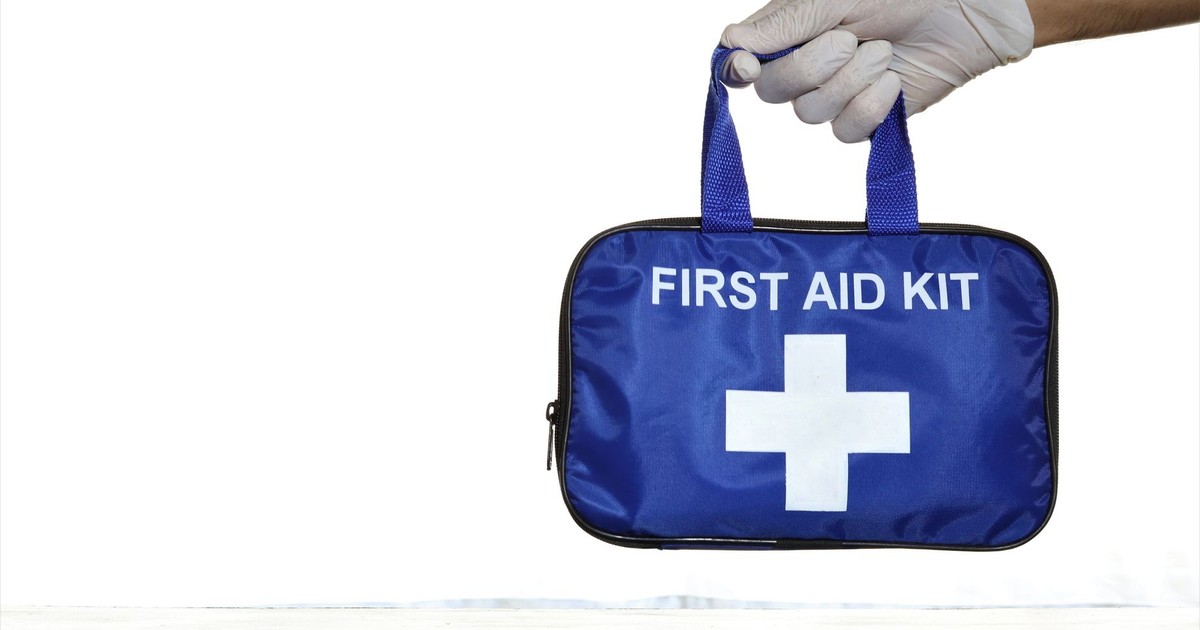 Close-up of a blue first aid kit held by a hand in a latex glove against an isolated white background.