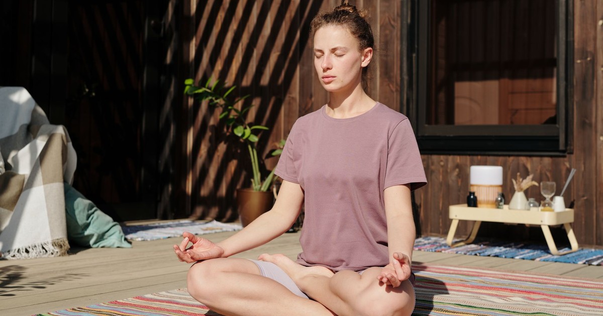 Woman practicing meditation in lotus pose on a sunny outdoor deck.