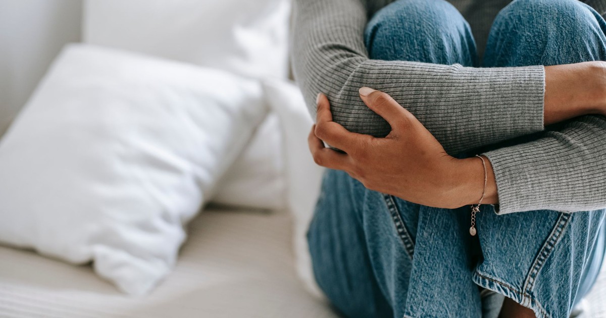 Crop faceless female feeling helpless and frustrated embracing knees while sitting on bed in loneliness