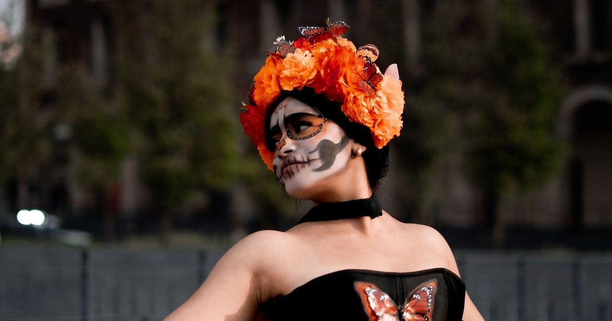 Woman dressed for Day of the Dead in festive makeup and flower crown, adorned with butterflies.