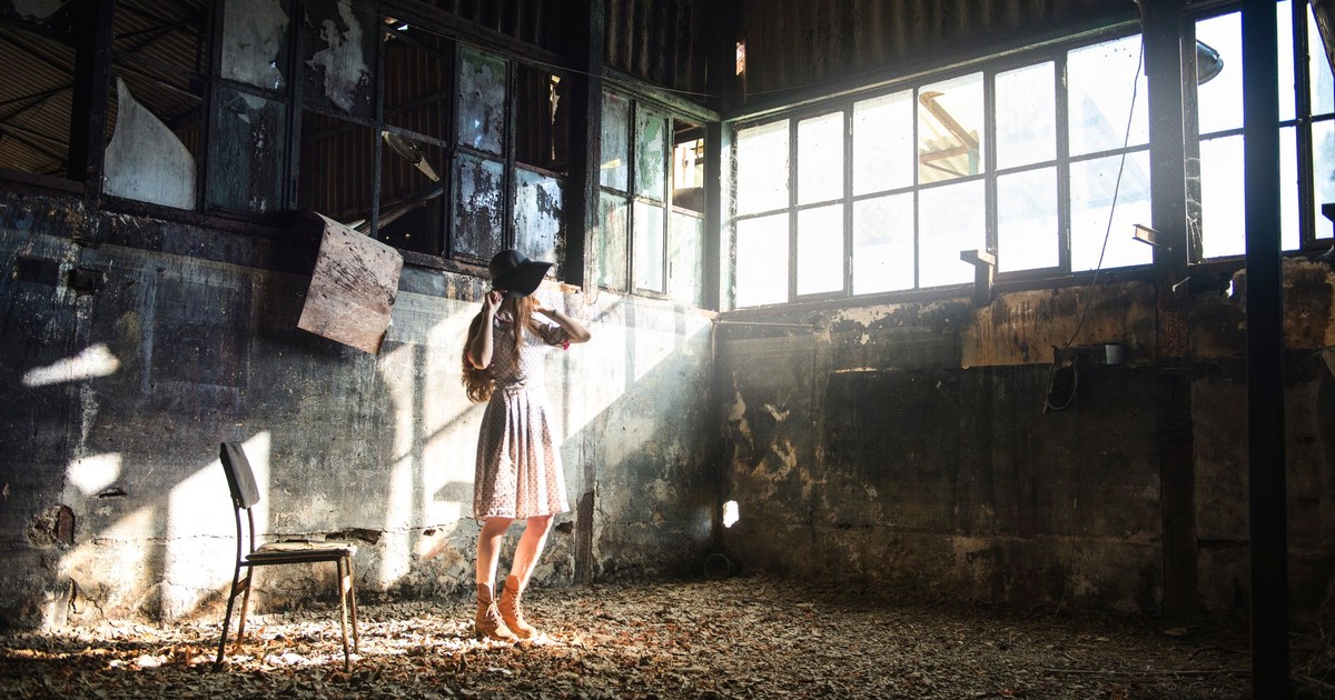 Full body of young anonymous female in trendy black hat looking away in sunshine in forgotten building