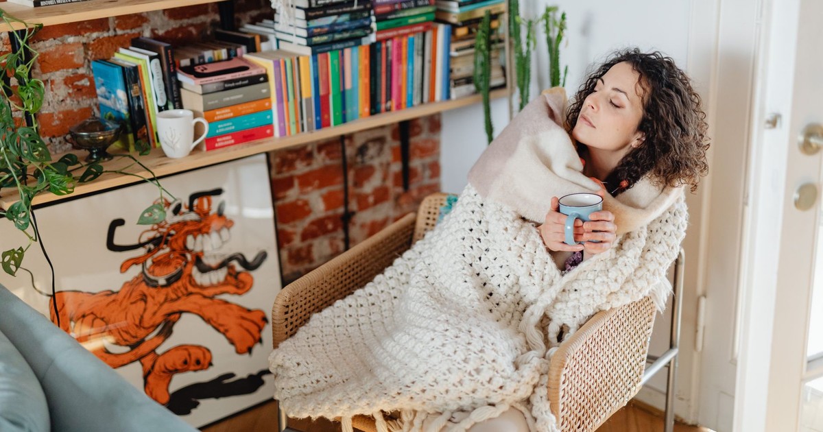 A woman with curly hair wrapped in a shawl, enjoying tea in a cozy home environment.