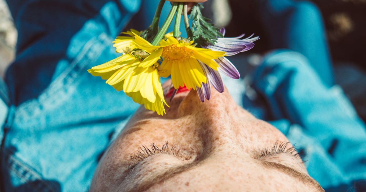 A freckled woman enjoys the aroma of colorful flowers in a bright outdoor setting.