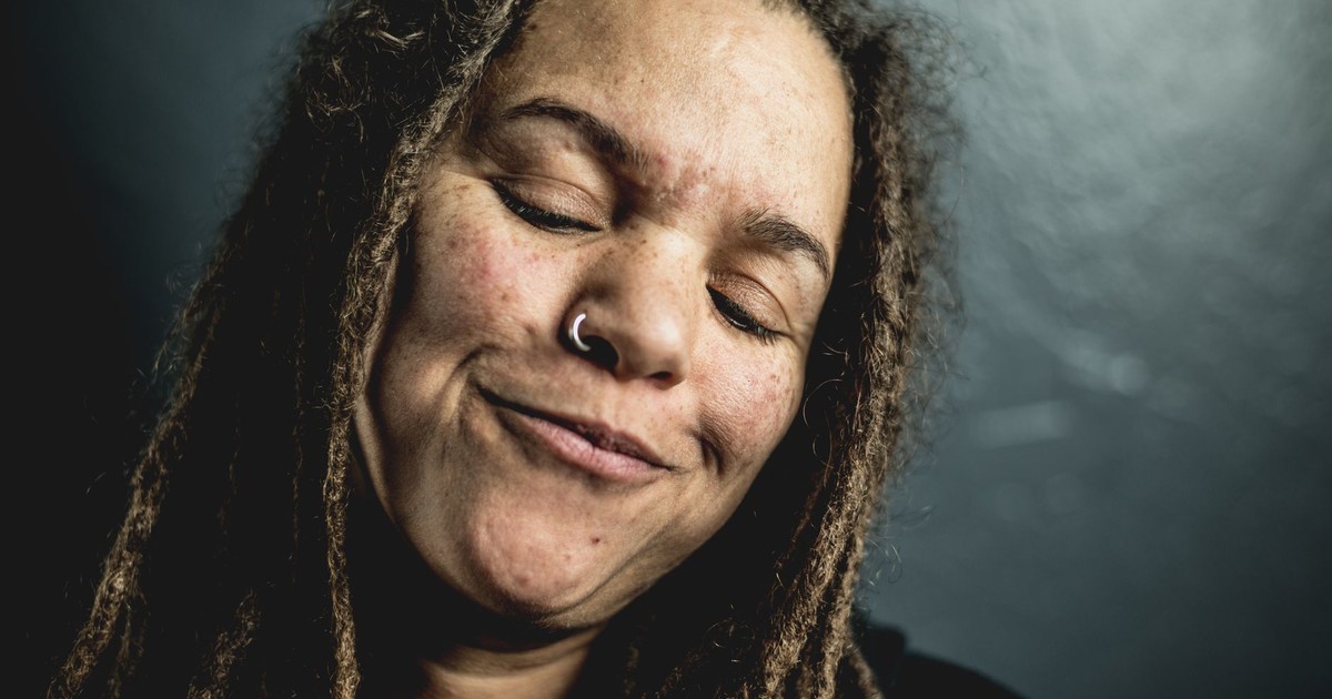 Close-up portrait of a woman with dreadlocks smiling peacefully with closed eyes.
