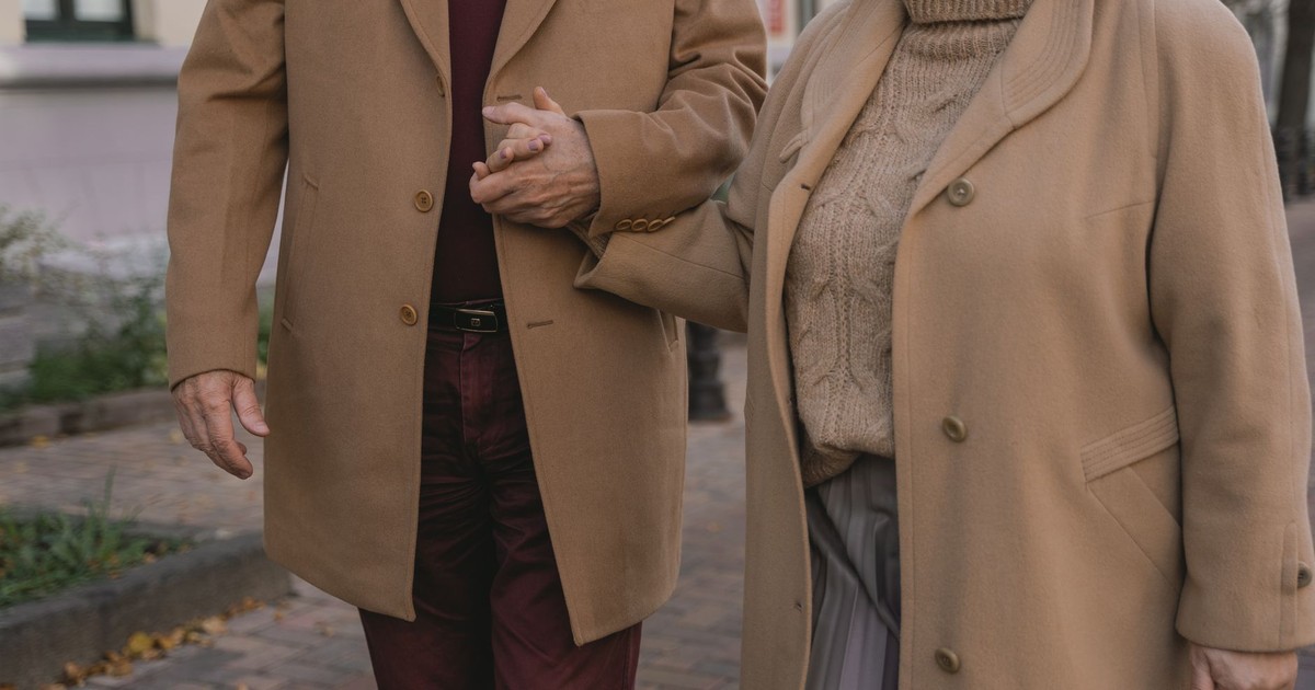 Senior couple holding hands while walking outside in autumn clothing, showcasing love and companionship.