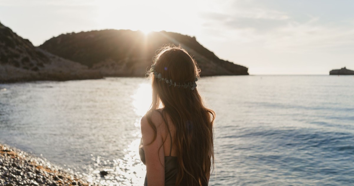 A woman with long hair gazes at the serene ocean during a summer sunset.