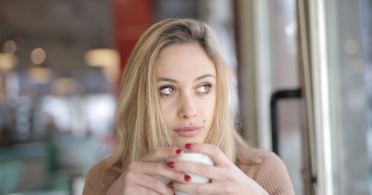 Close-up of a young woman holding a coffee cup, lost in thought indoors.