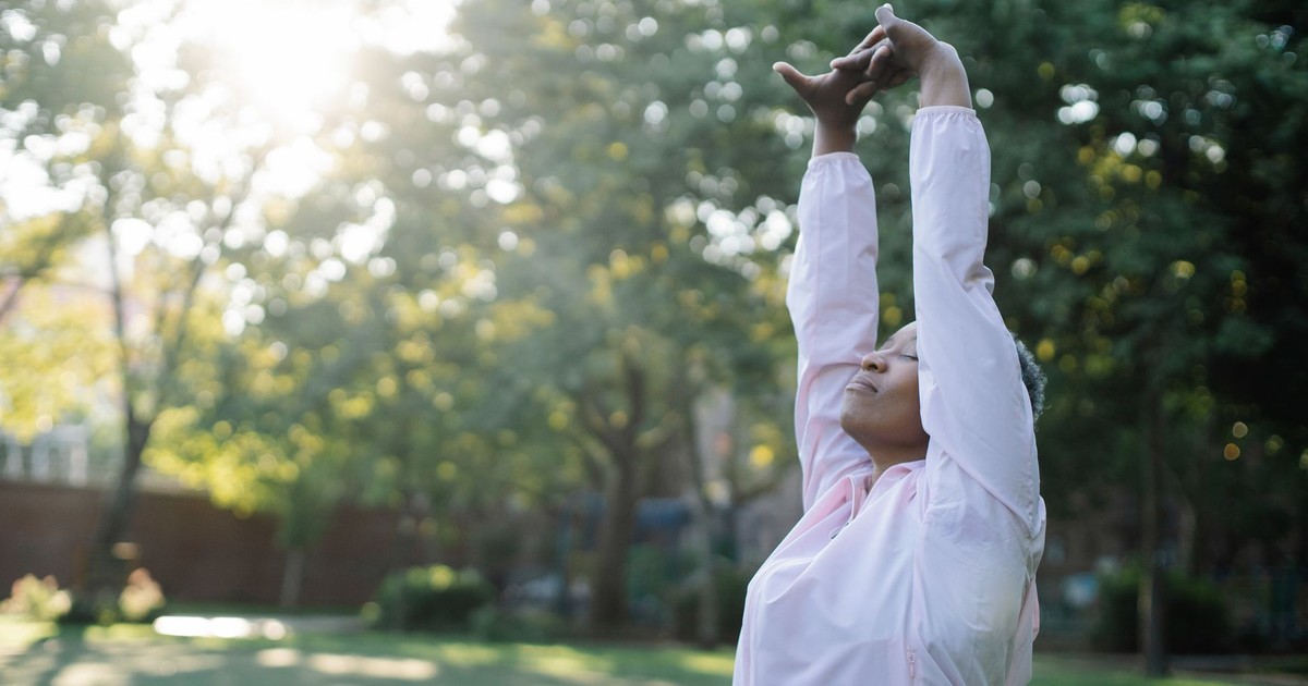 Woman enjoying a stretch in a peaceful, sunlit park setting outdoors.