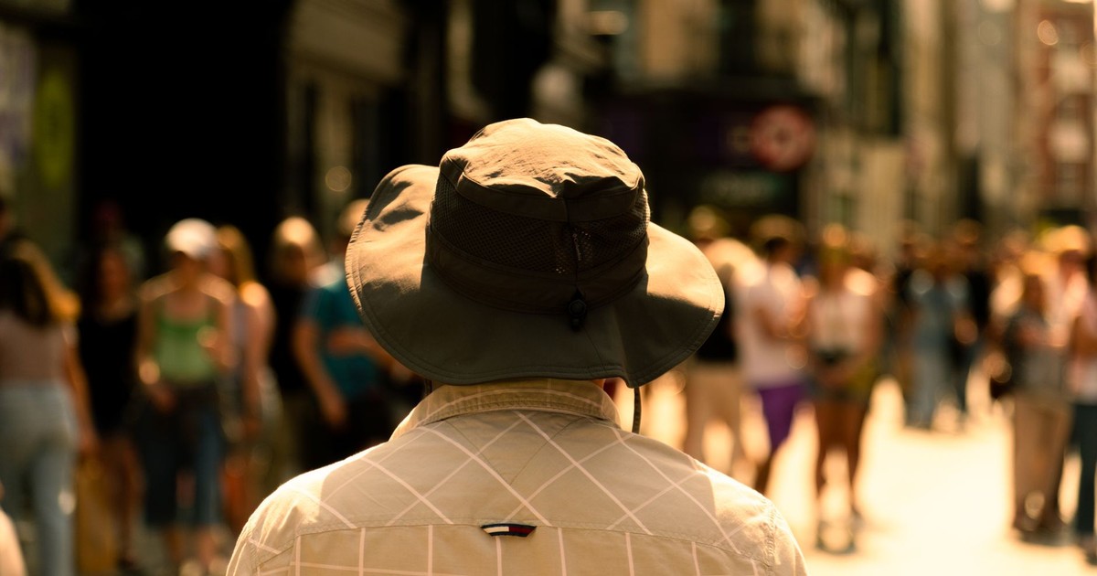 A scenic urban street capture featuring a sunlit pedestrian wearing a wide-brimmed hat during late summer.