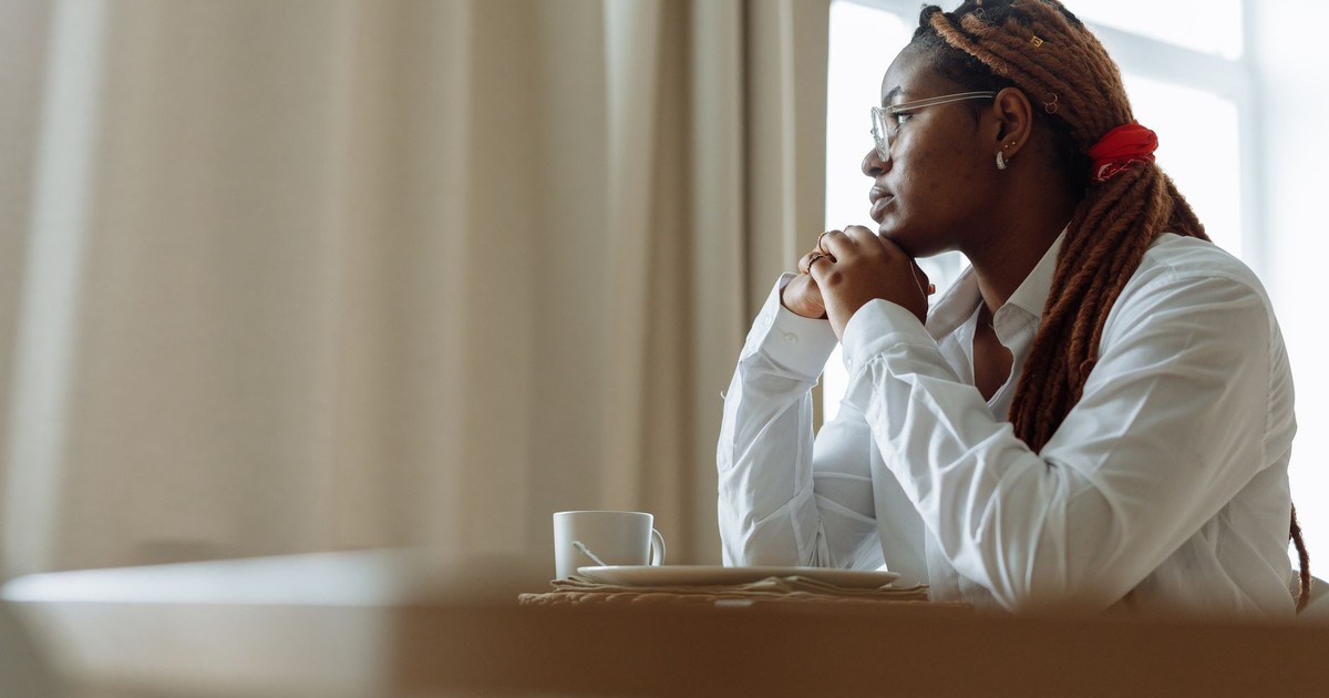 Side view of a pensive person with dreadlocks in a white shirt, enjoying coffee indoors.