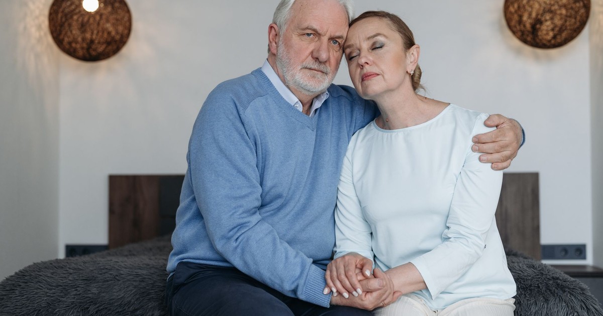 Senior couple sharing a comforting embrace, conveying love and support in a serene bedroom setting.